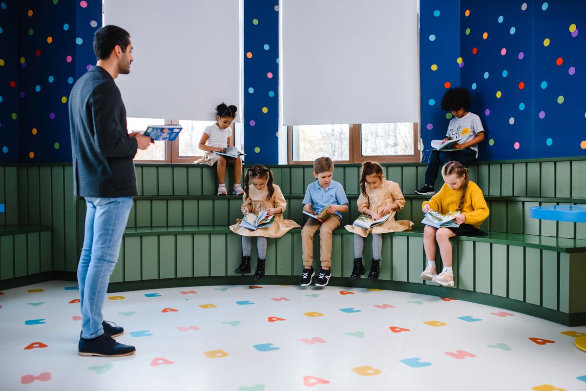 孩子们阅读图书、教师在旁手持平板的示例照片